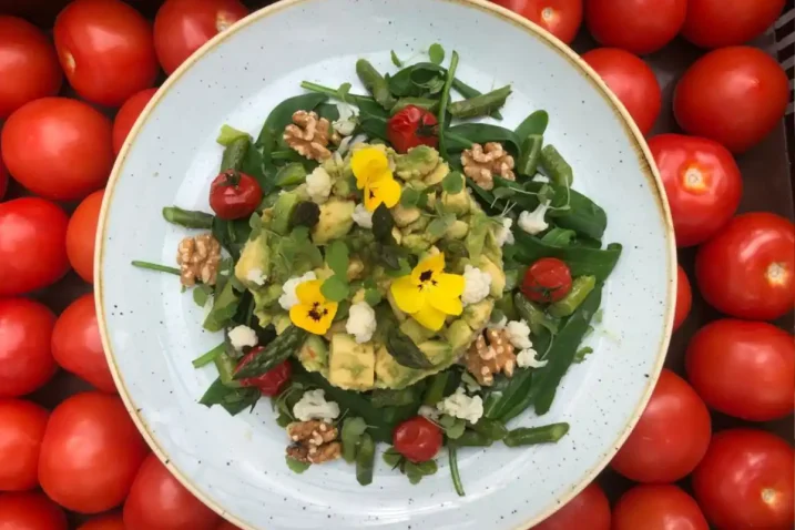 Vegetarisch gerecht rijkelijk bekleed met groenten en eetbare bloemetjes. Het bord staat op cherry tomaatjes wat voor een leuk contrast zorgt.